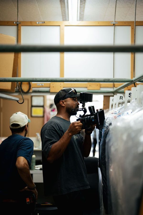 Camera operator shooting handheld between racks of clothes while a crew member looks on