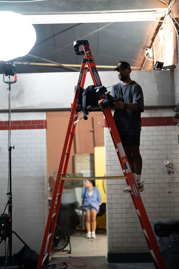 Crew member on a red ladder rigging a light above a tiled hallway set
